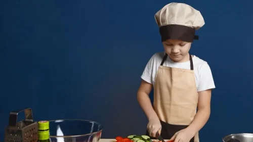 focused-male-child-chef-apron-hat-slicing-vegetables-vegetarian-lasagne_343059-183_11zon